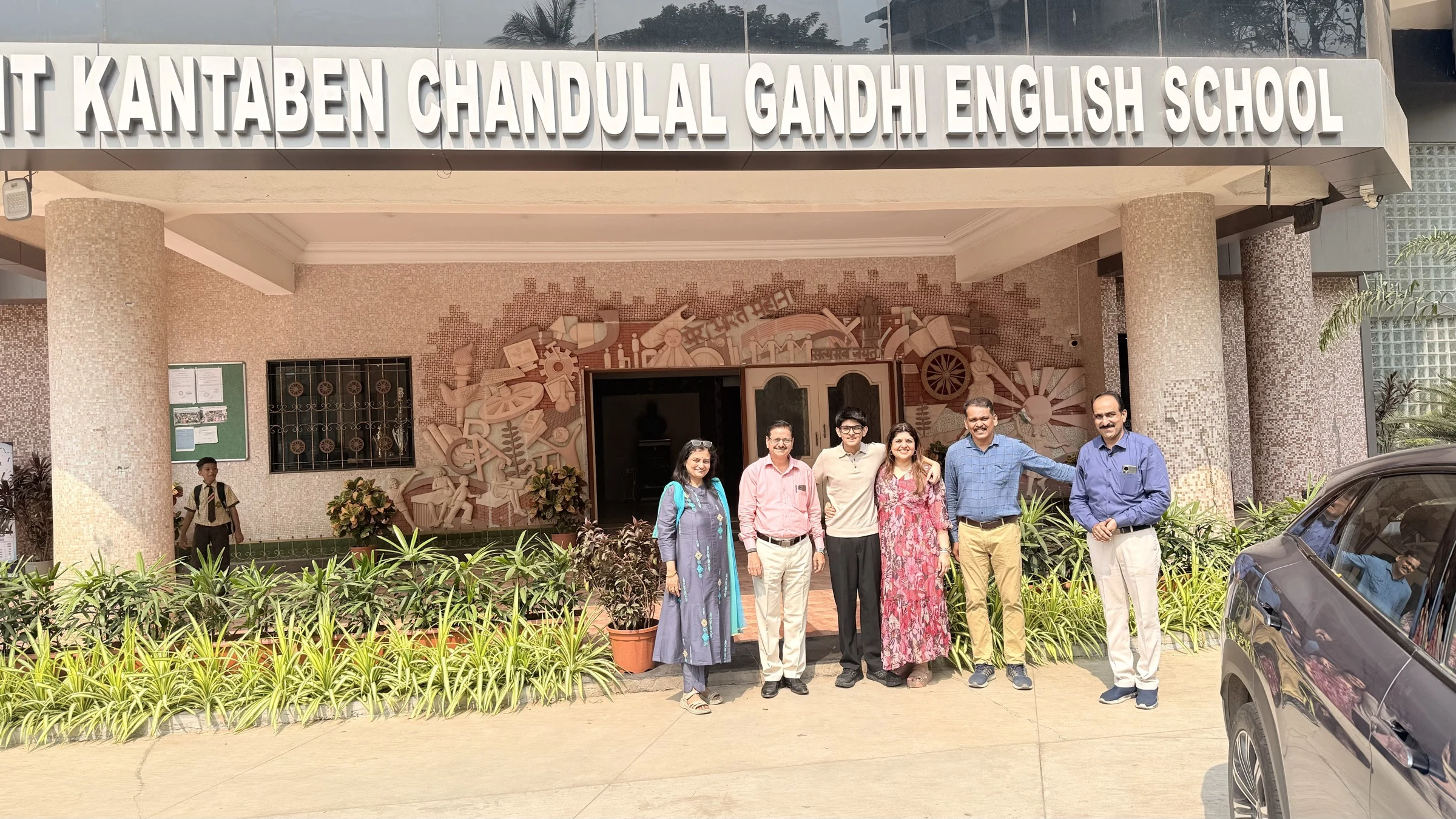 Aarav with school representatives outside KC Gandhi School, with the school name visible